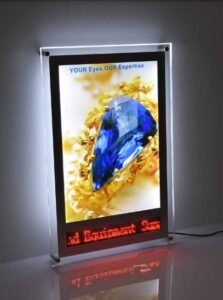 A BLUE DIMOND PENDENT IN A GOLD COVERED SHOWING IN A FABRIC LIGHT BOX BY SIGNEX